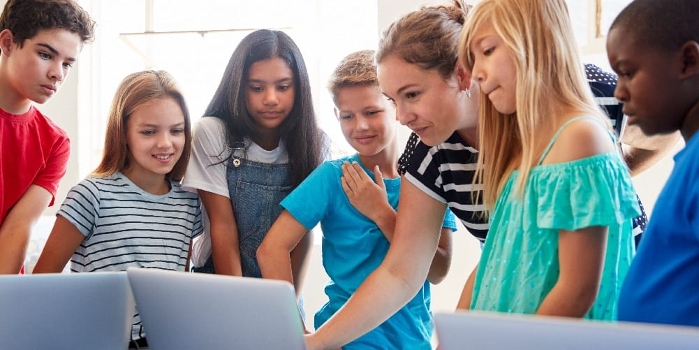 Centegix Blog August 4-4- _2 A teacher pointing to a laptop screen surrounded by her young students.