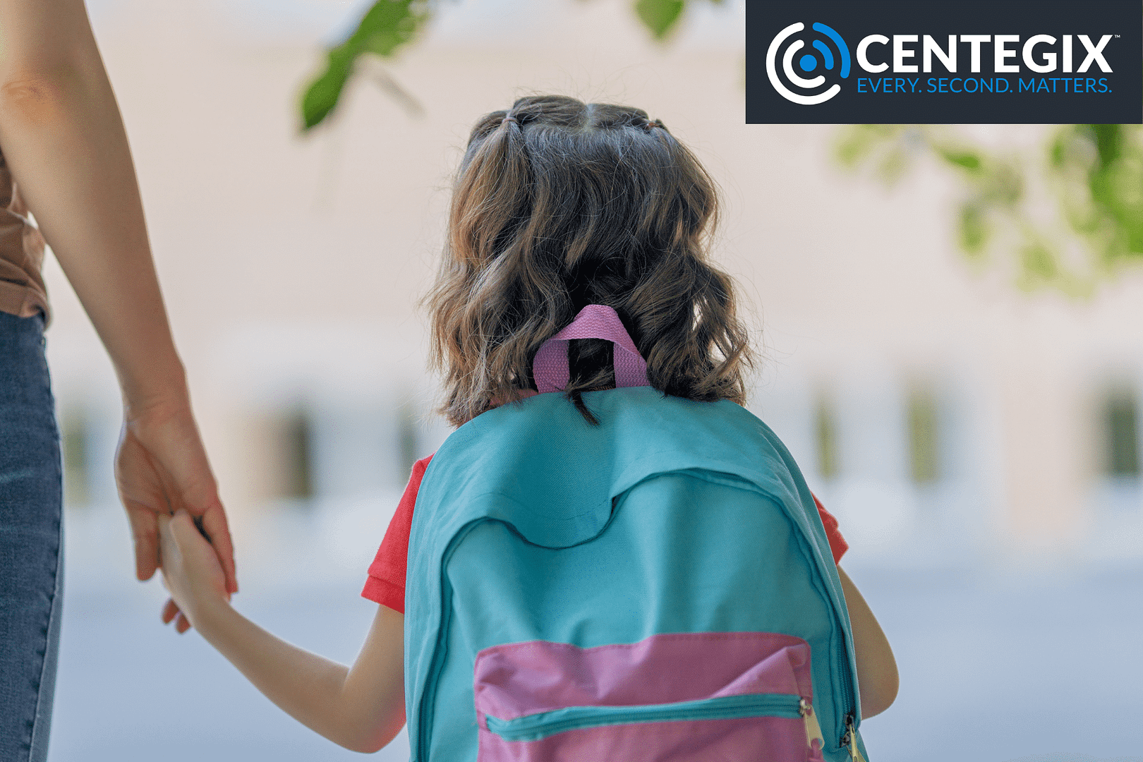 A young girl wearing a backpack holding an adult's hand outside