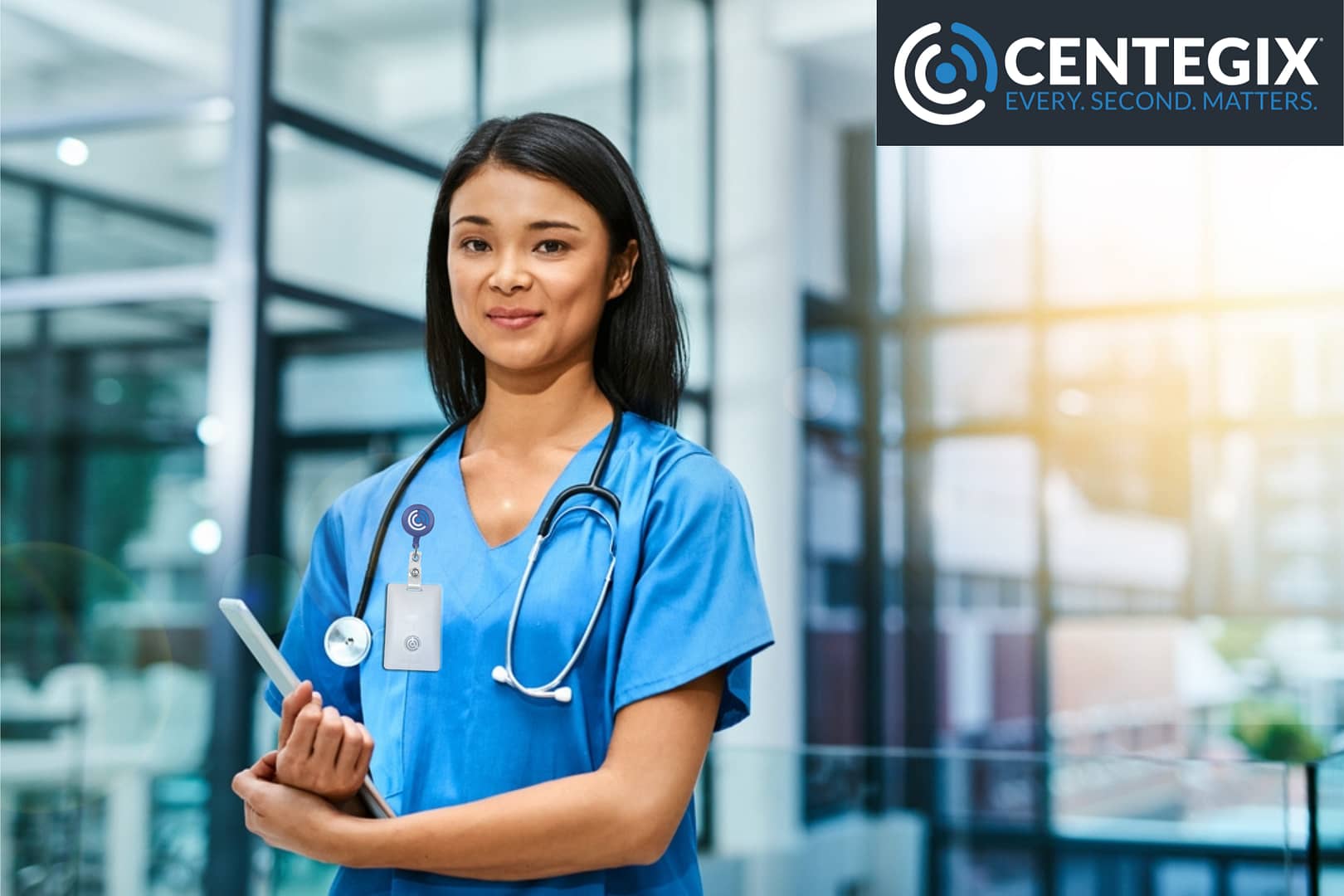 A young nurse is standing in a hospital atrium wearing a CrisisAlert wearable duress button by CENTEGIX.