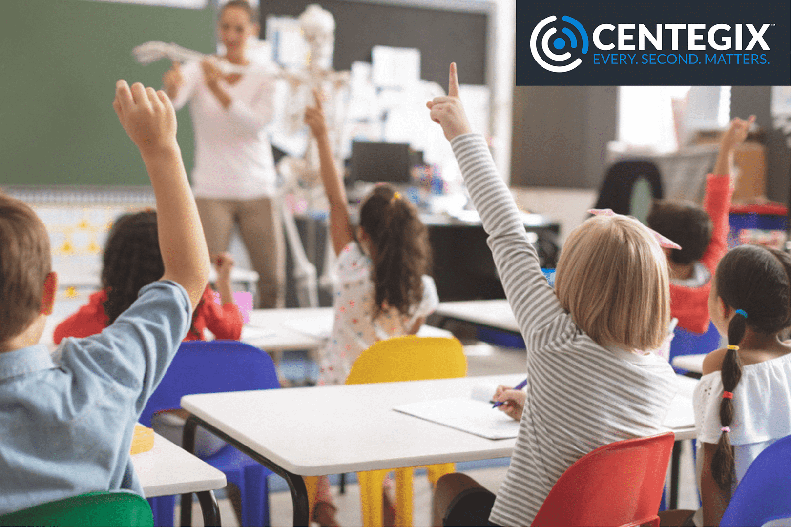 A group of elementary students in a classroom raising their hands.