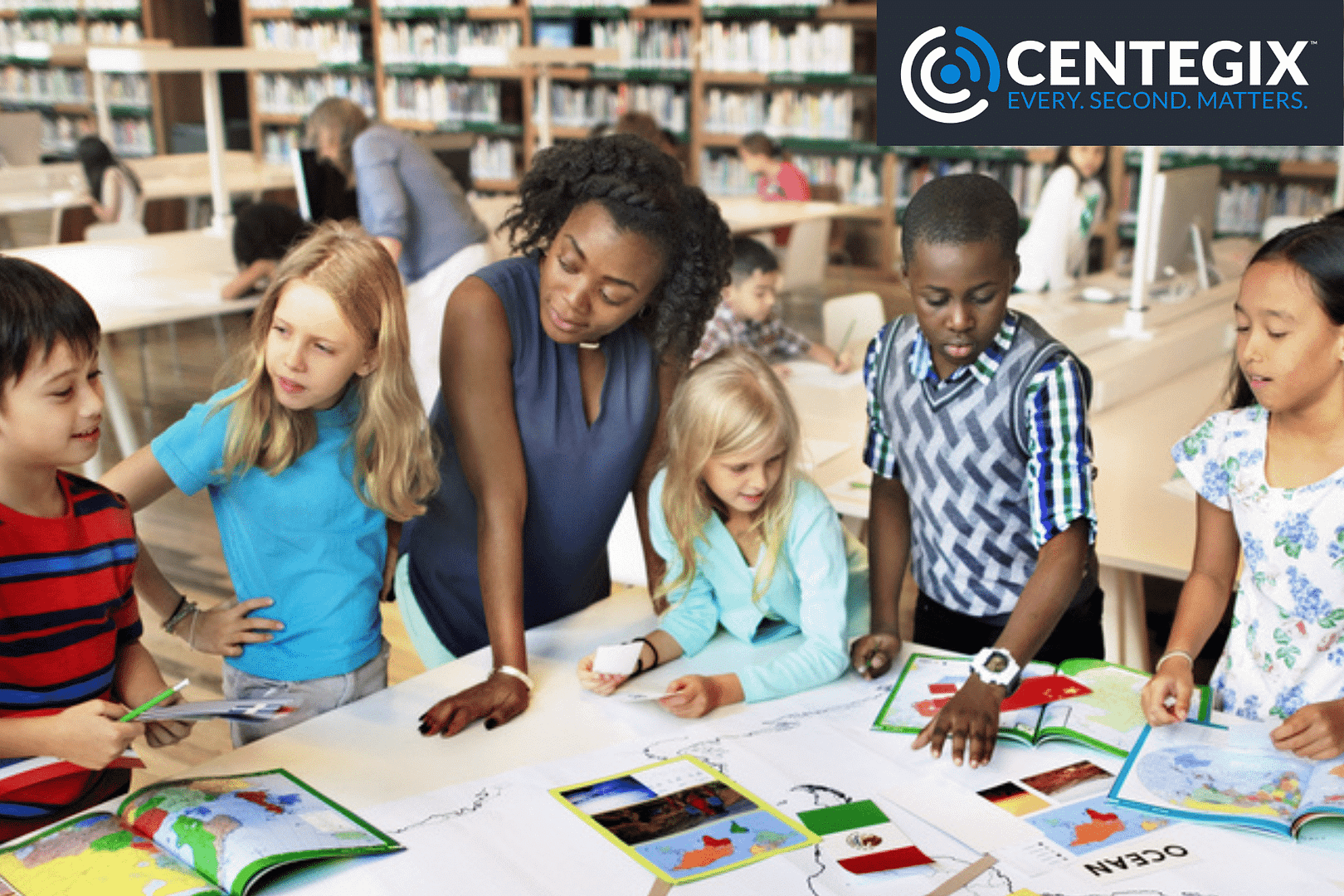 A diverse group of students gathered around a table with their teacher working on a world geography project in a library.