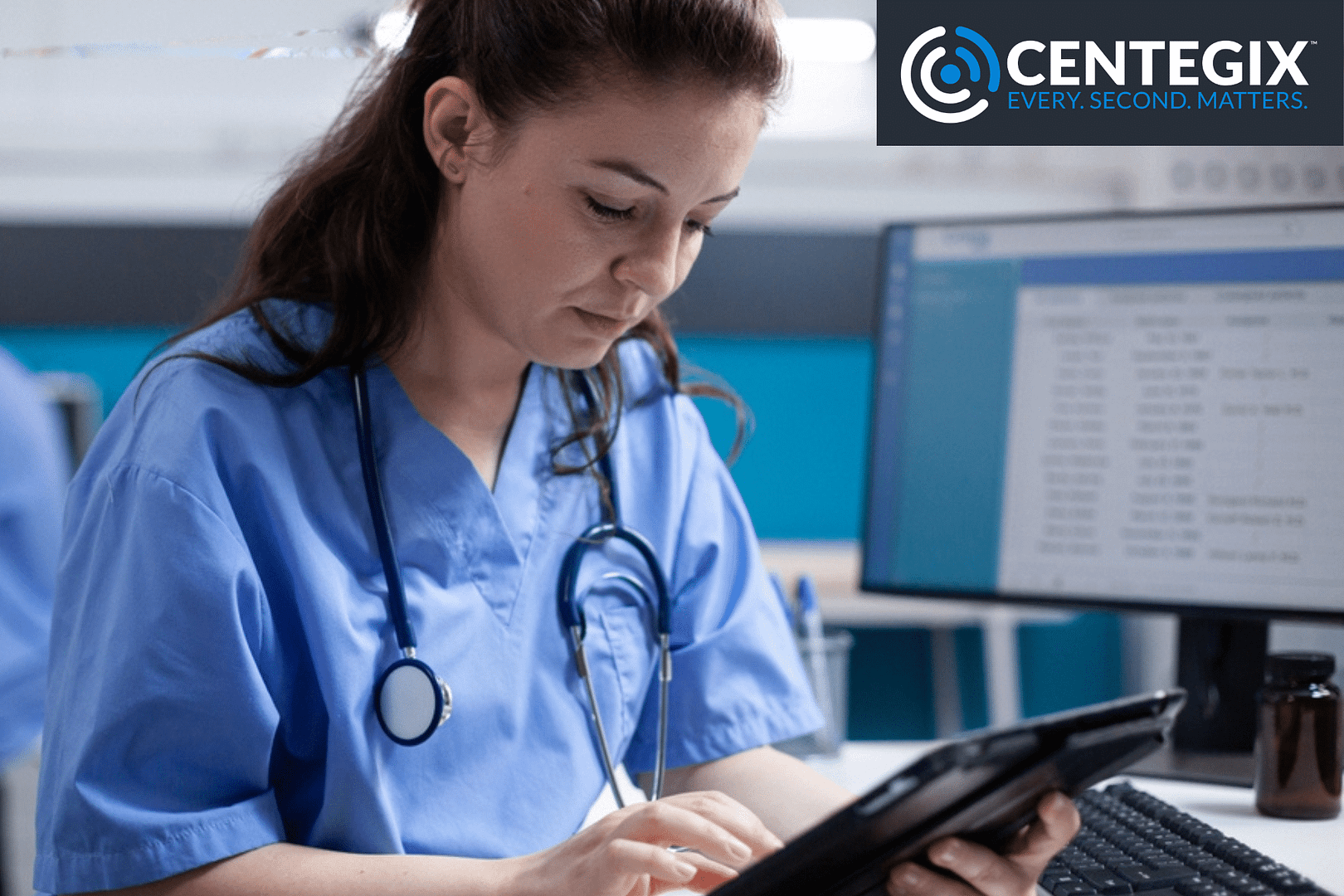 Nurse sitting at a nursing station reviewing something on a tablet.