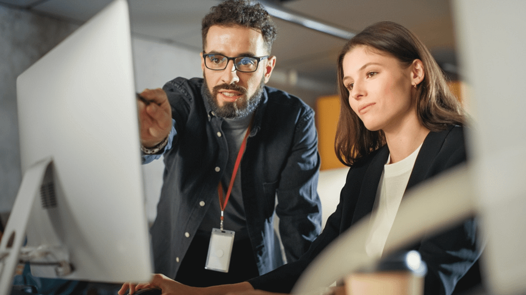 Two professionals looking at a computer together with one pointing at the screen.
