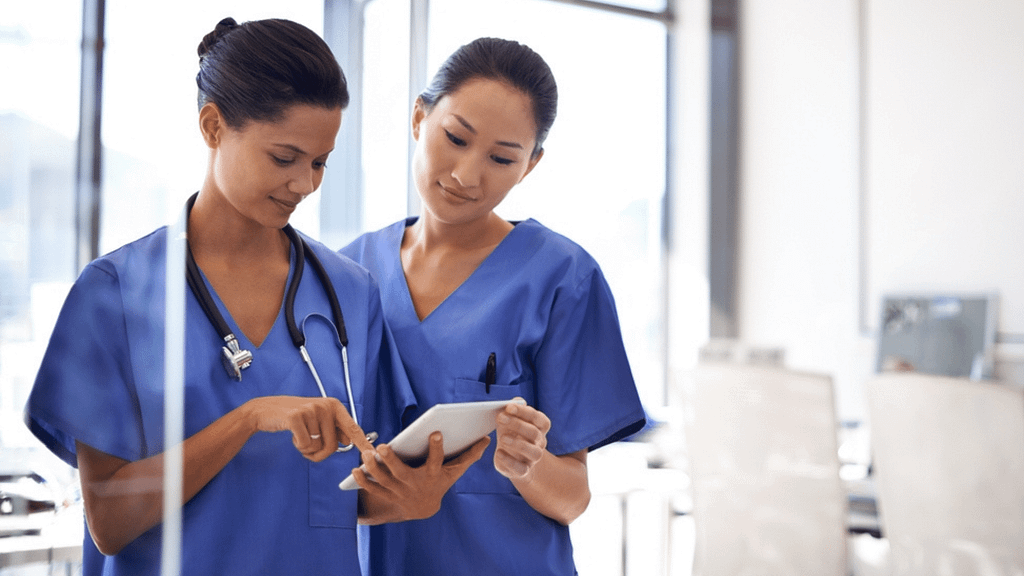 Two female nurses standing together looking at something on a tablet.