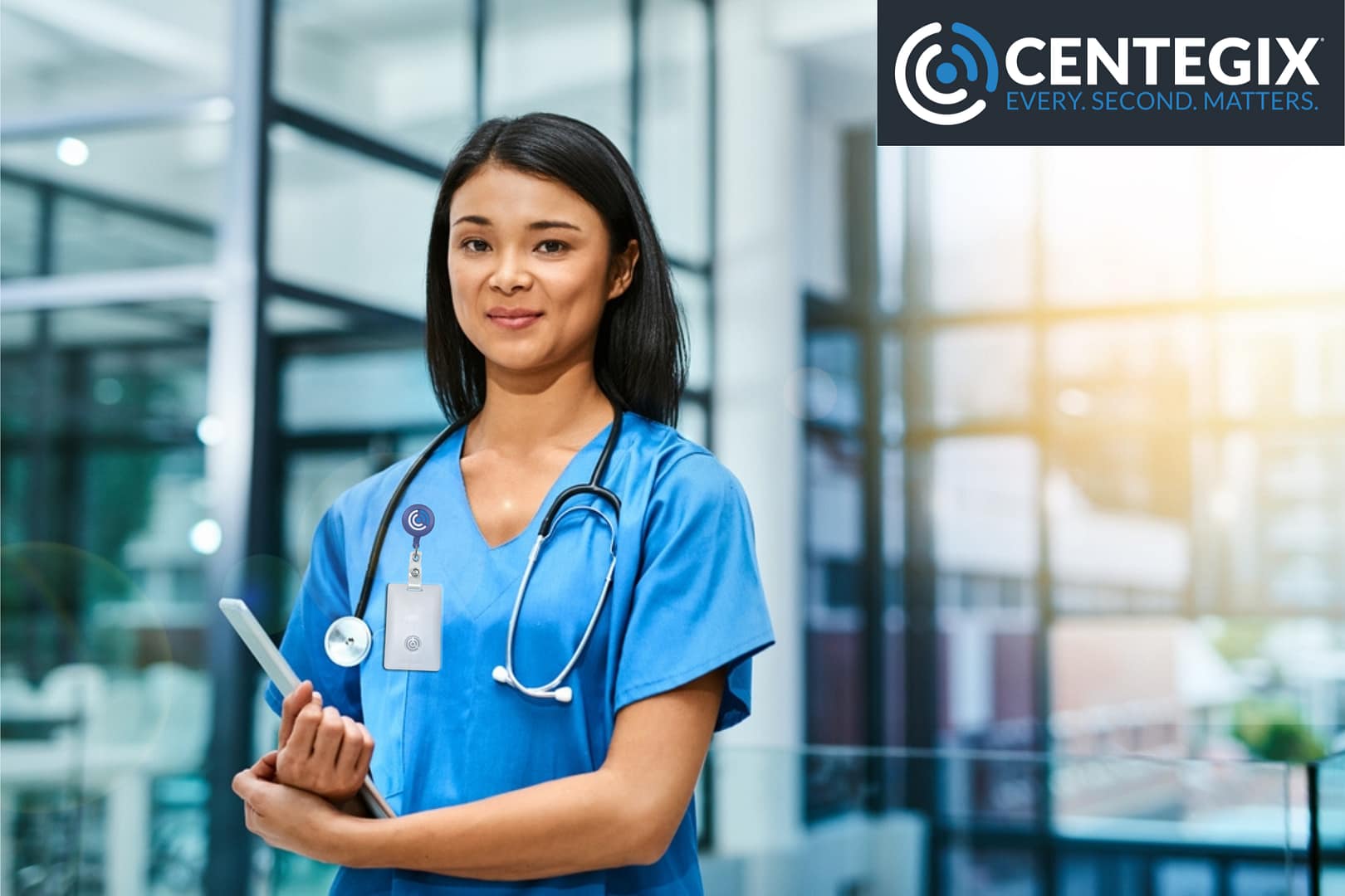 violence in healthcare A young nurse is standing in a hospital atrium wearing a CrisisAlert wearable duress button by CENTEGIX.